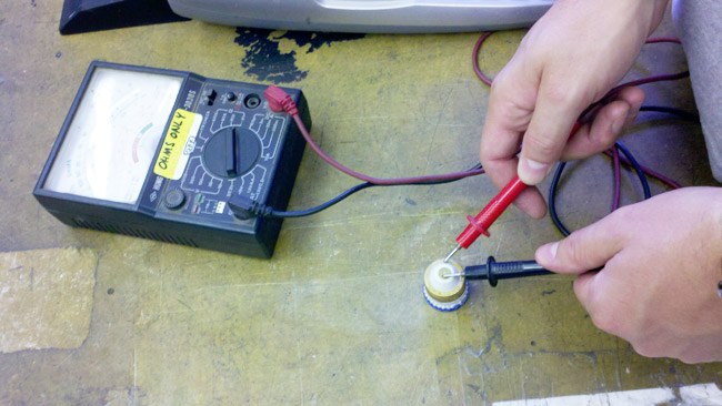 Hands testing a small electrical part with a meter on the workbench