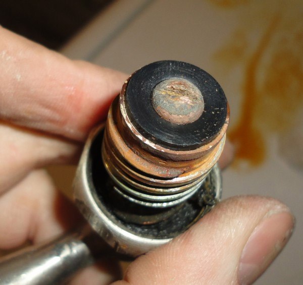 Hand holding a worn faucet stem and washer assembly close up
