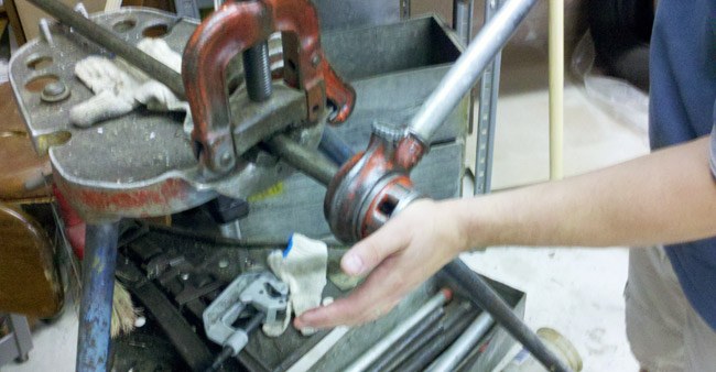 Hands threading a pipe held in a vise at Heights Hardware
